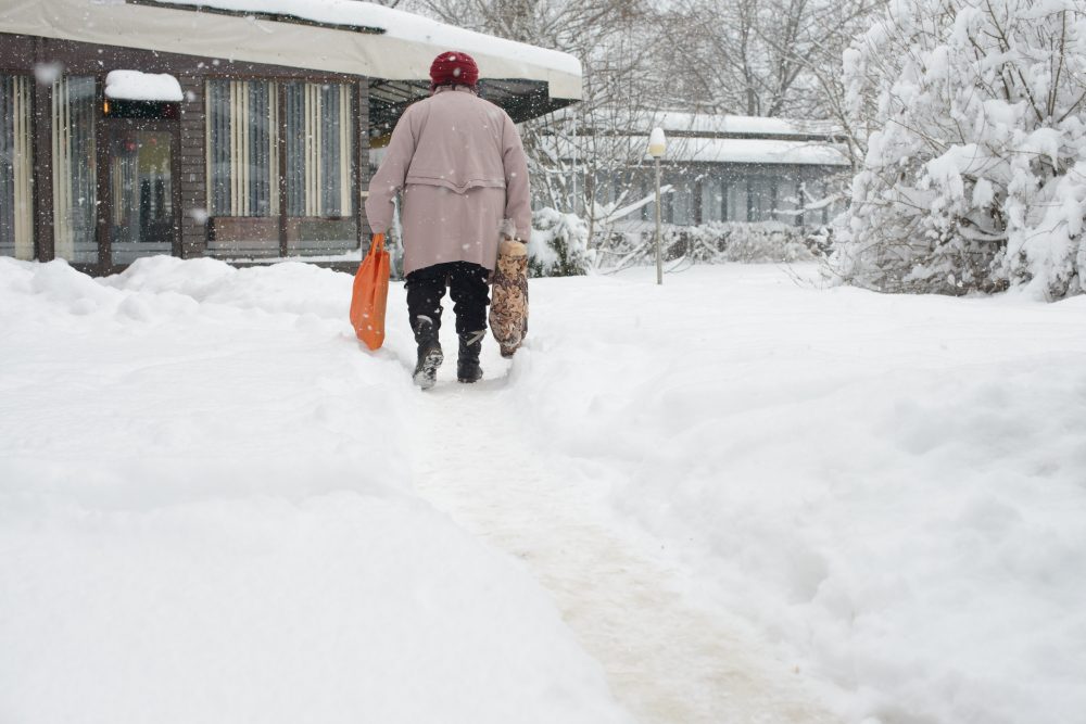 Older adult walking alone on a narrow snow-covered walkway in winter, highlighting fall risk and home safety concerns