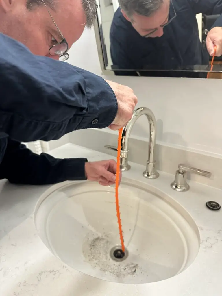 Removing hair from a bathroom sink drain using a plastic hair removal strip during a Good Company maintenance visit in North York