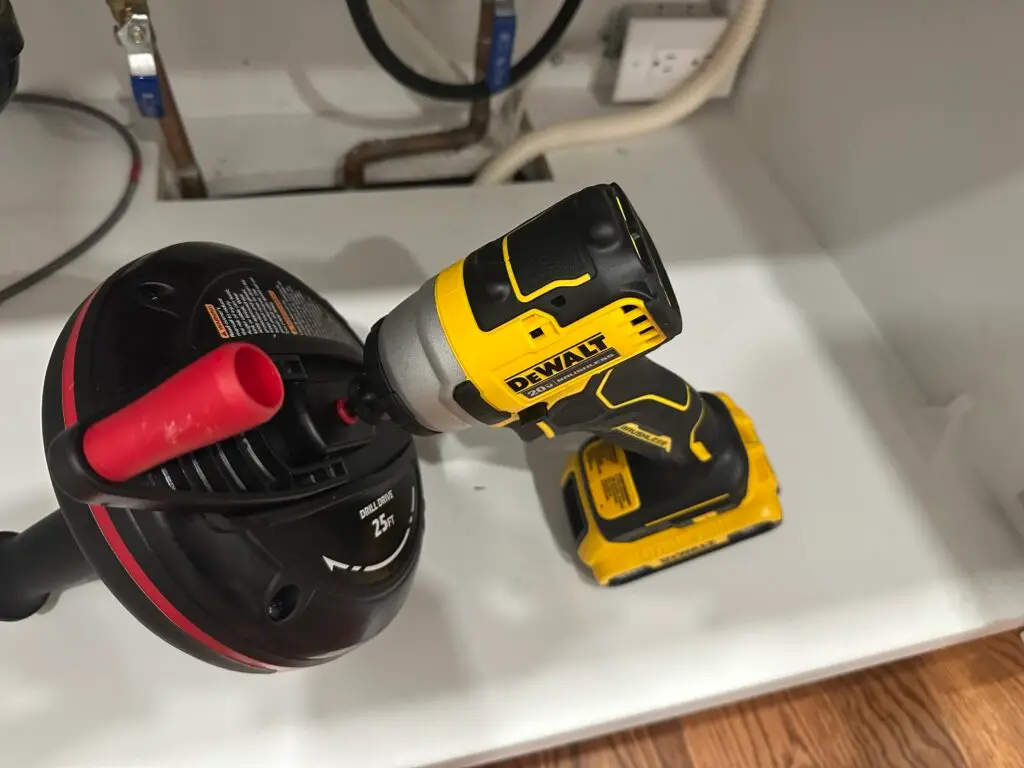 Close up of a DeWalt drill connected to a handheld drain auger for clearing a clogged kitchen sink