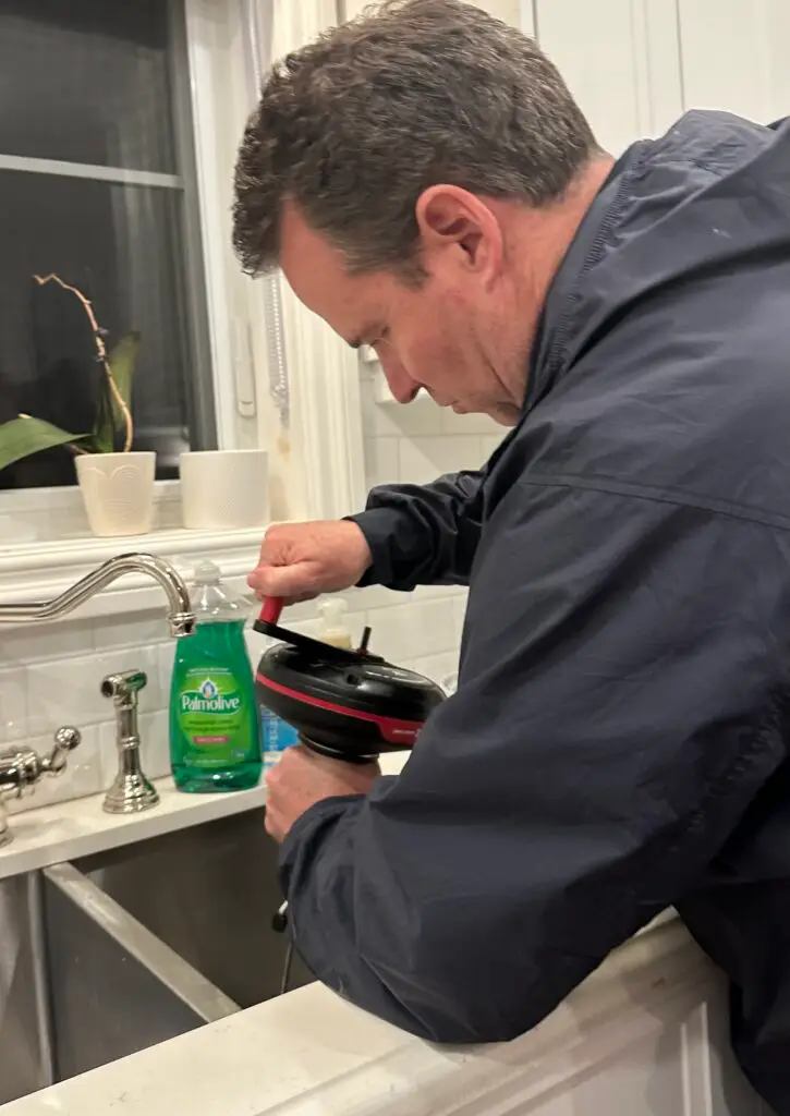 Clearing a clogged kitchen sink from above using a hand powered drain snake