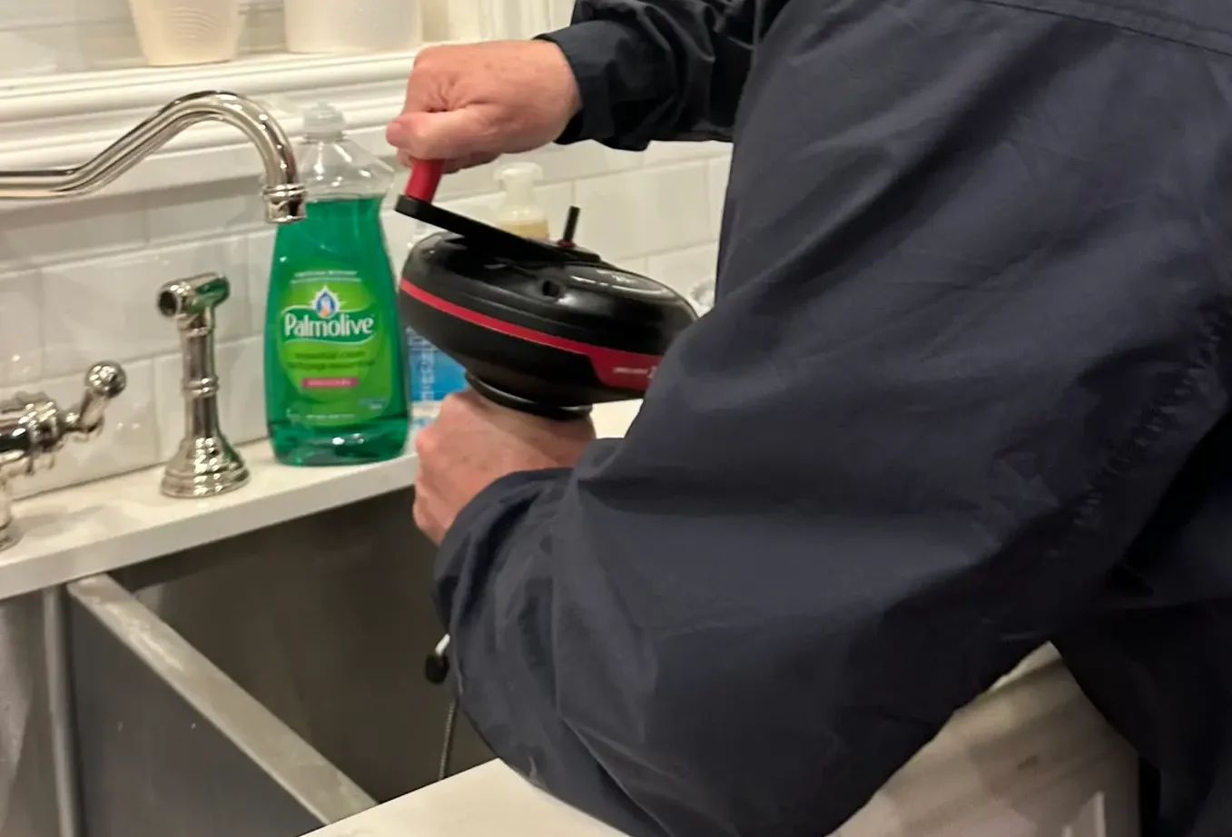 Clearing a clogged kitchen sink from above using a hand powered drain snake