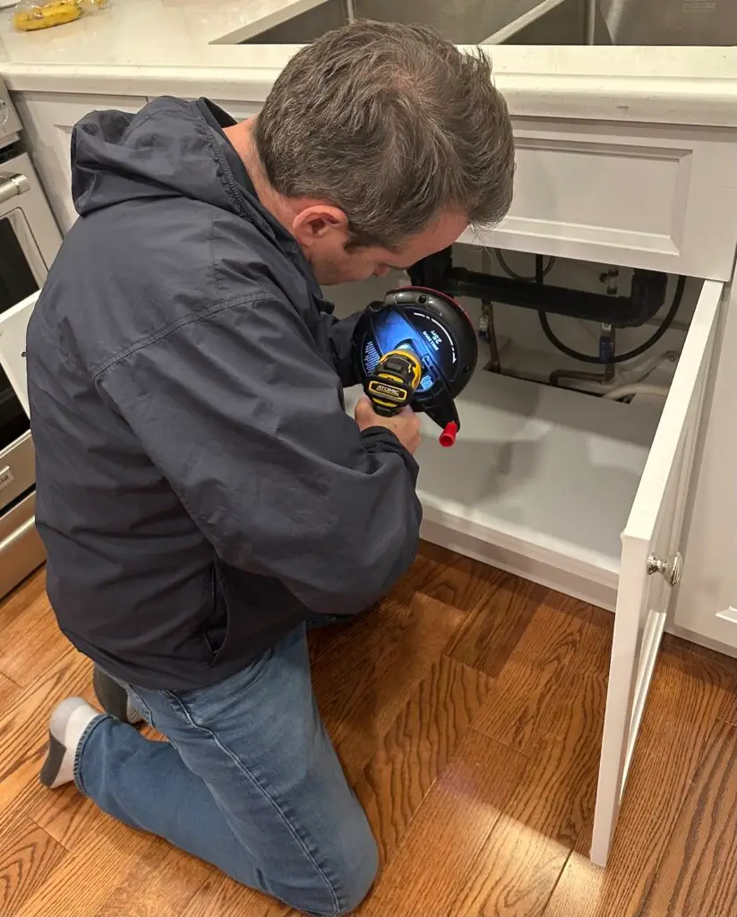 Snaking a kitchen drain from under the sink using a handheld auger in a Toronto home