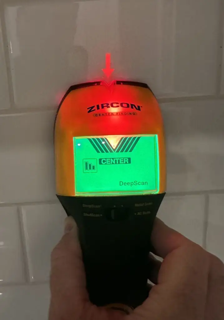 Stud finder reading on a glossy subway tile backsplash to identify studs and avoid plumbing and electrical lines.