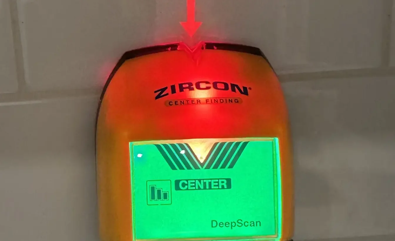 Stud finder reading on a glossy subway tile backsplash to identify studs and avoid plumbing and electrical lines.