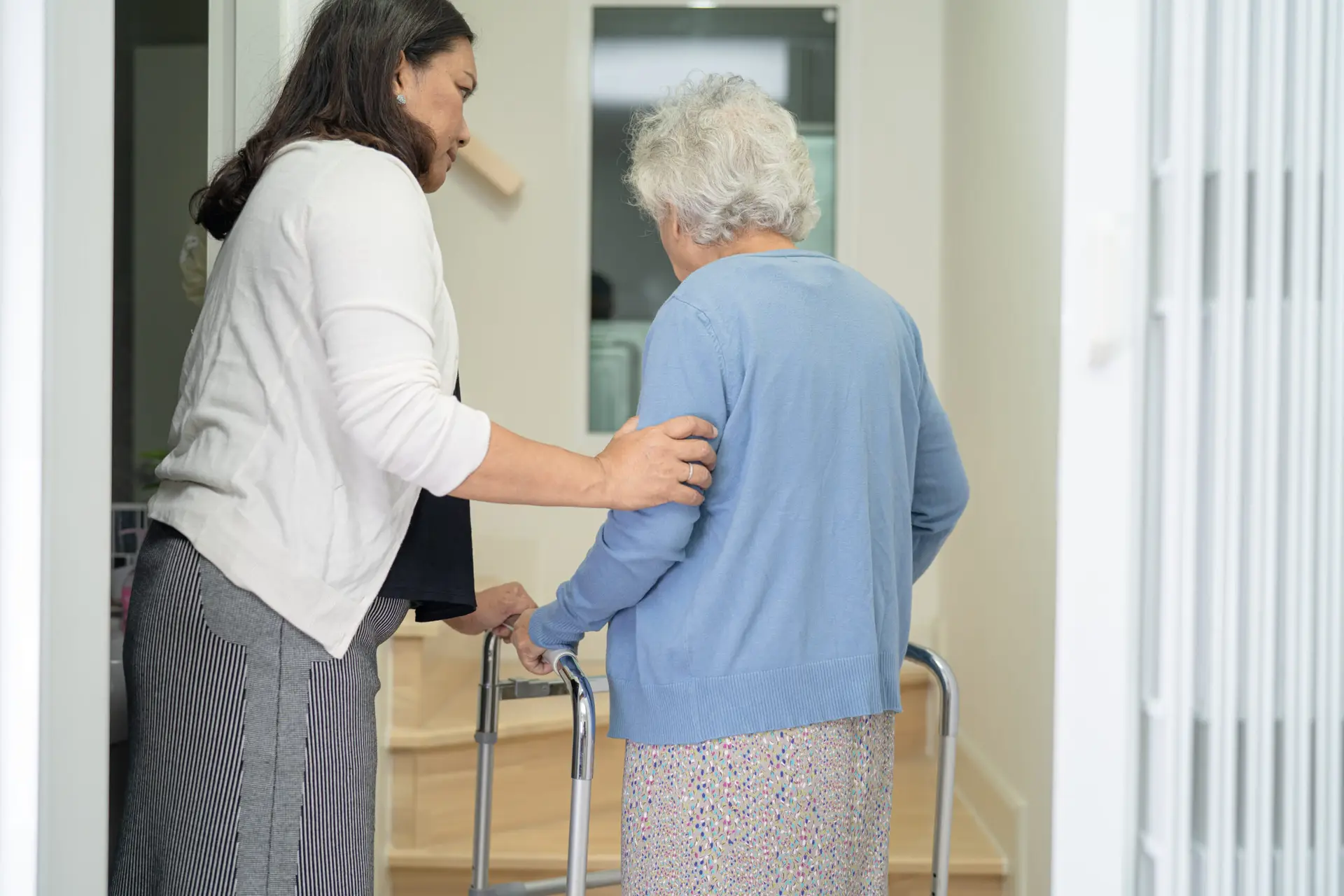 Caregiver assisting older woman walking safely indoors with a walker