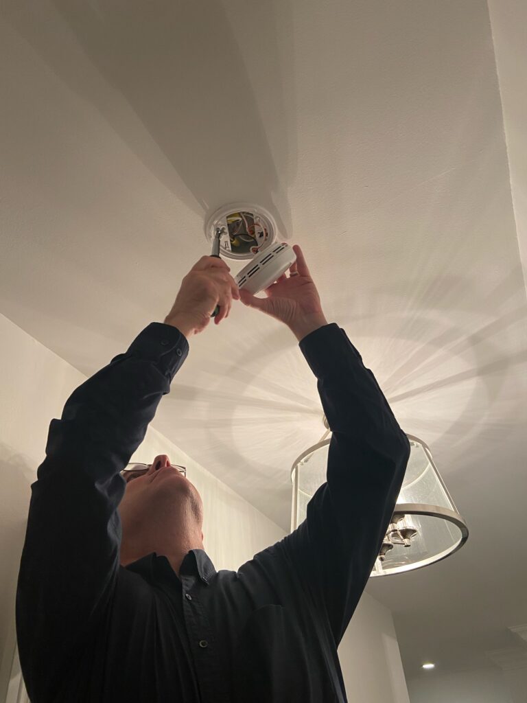 Technician installing a hardwired smoke detector on a ceiling in a Toronto home