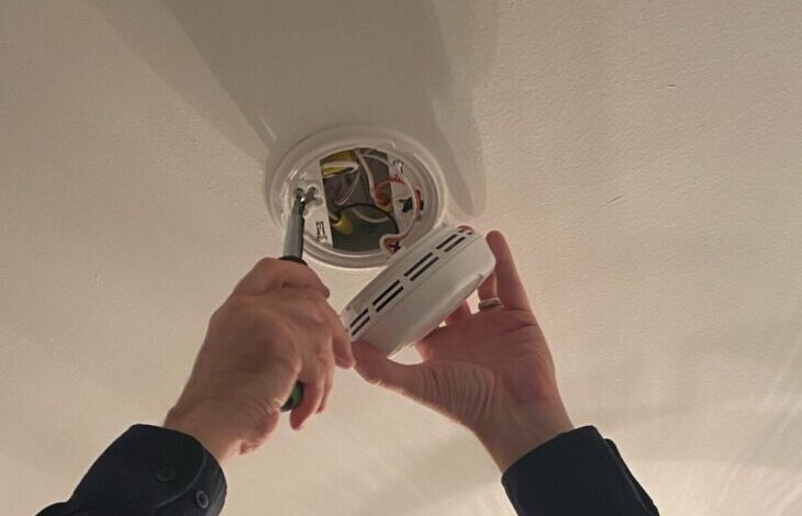 Technician installing a hardwired smoke detector on a ceiling in a Toronto home
