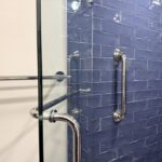 Grab bar installation in Toronto shower with vertical safety bar on blue tile wall beside glass door