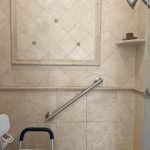 Diagonal grab bar installed beside a shower bench in a travertine tiled shower to provide comfortable support and stability.