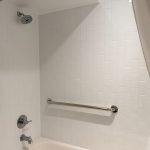 Chrome grab bars installed in a white tiled tub and shower to improve bathroom safety and accessibility in Toronto.