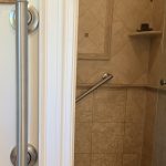 Vertical entry grab bar and diagonal shower grab bar installed in a travertine shower to improve bathroom safety and accessibility in Toronto.